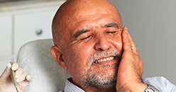 Man in dental chair holding his cheek in pain