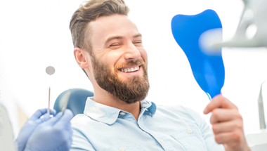 Man in dental chair looking at smile in mirror