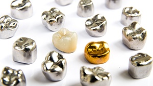 A tooth-colored and gold dental crown in the middle of several silver ones