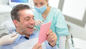 Man smiling at his reflection next to dentist