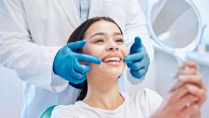 Dentist pointing to patient’s teeth as she smiles at reflection in mirror