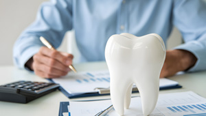Man in blue shirt calculating invoices at desk next to large model tooth