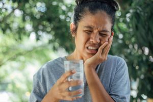 person drinking a glass of ice water outside and experiencing tooth sensitivity 