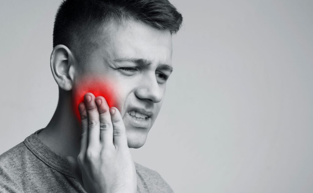 Grayscale image of man pressing hand to red inflamed jaw