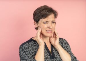 Grimacing woman touching her jaw joints 